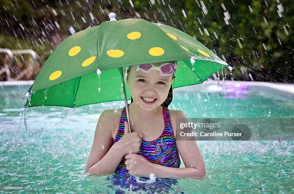 A smiling girl and umbrella in a pool in the rain