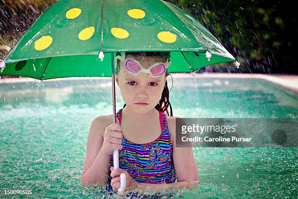 sad girl holding an umbrella in a pool as it rains - bad luck stock pictures, royalty-free photos & images