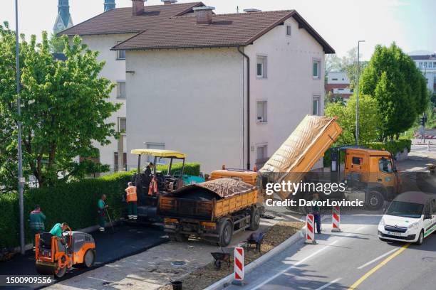 road construction works with workers controlling the process in which truck with hat asphalt is pouring the asphalt into asphalt paving machine which is covering and leveling the street with new asphalt. - asphalt paving machine stock pictures, royalty-free photos & images