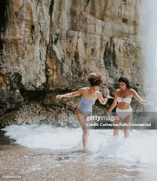 two young woman frolic in the surf on an amazing beach - love on the rocks stock pictures, royalty-free photos & images