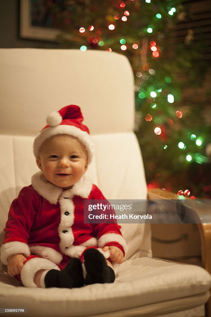 Adorable baby boy wearing santa outfit smiles.