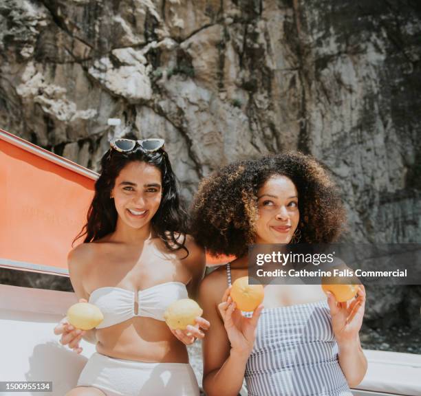 two pretty young woman comically hold citrus fruits over their chests and make funny faces - seno fotografías e imágenes de stock