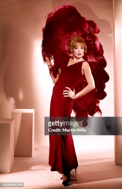 American comedienne, actress, singer and businesswoman Edie Adams poses for a portrait in high heels, red dress and a feathered fan in Los Angeles,...