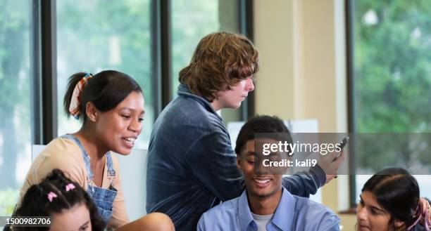 teenage boy looks serious in group of happy friends - alone in a crowd sad stockfoto's en -beelden