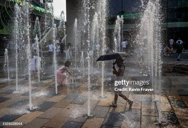 Girl carries an umbrella as she walks through a water fountain at shopping mall to cool off during a heatwave on June 23, 2023 in Beijing, China....