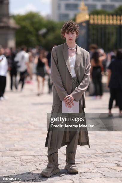 Daniel Millar is seen wearing a beige brown shoulder pad blazer, white tanktop, silver chain, matching buckle belt and matching suit pants and plisee...