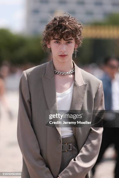 Daniel Millar is seen wearing a beige brown shoulder pad blazer, white tanktop, silver chain, matching buckle belt and matching suit pants and plisee...