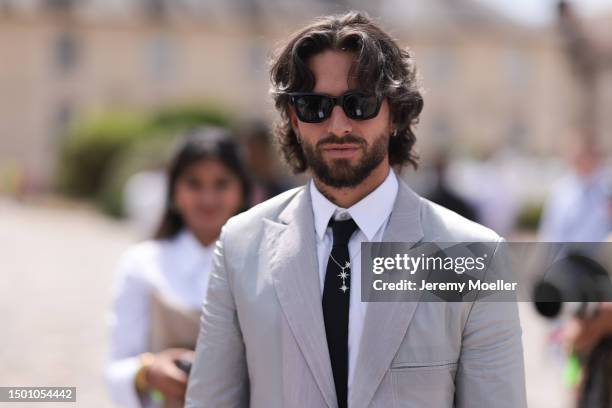 Maluma is seen wearing a grey suit with blazer and grey suit pants, black shades, black tie, silver chain and olive leather Dior saddle bag outside...