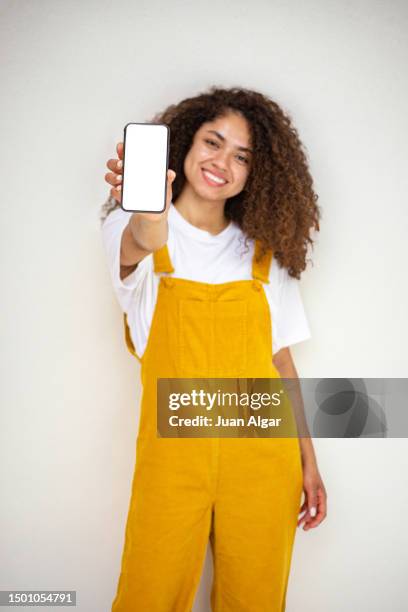 delighted young ethnic woman showing smartphone and smiling in studio - showing mobile stock pictures, royalty-free photos & images