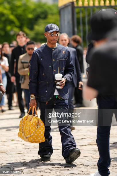 Pharrell Williams wears a navy blue denim with large white embroidered pattern cap, silver and gold rhinestones small circle sunglasses from Louis...