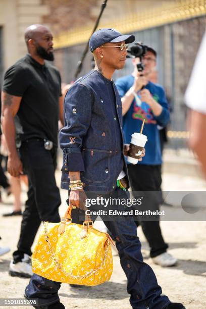 Pharrell Williams wears a navy blue denim with large white embroidered pattern cap, silver and gold rhinestones small circle sunglasses from Louis...