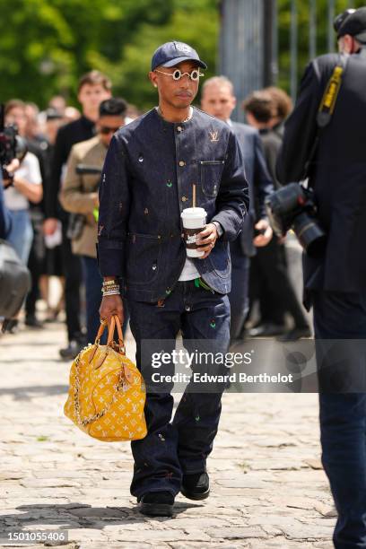 Pharrell Williams wears a navy blue denim with large white embroidered pattern cap, silver and gold rhinestones small circle sunglasses from Louis...