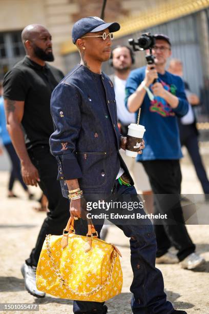 Pharrell Williams wears a navy blue denim with large white embroidered pattern cap, silver and gold rhinestones small circle sunglasses from Louis...