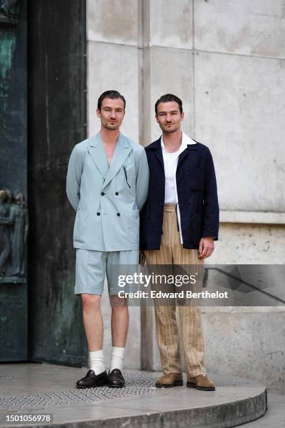 Brett Staniland wears a pale blue blazer jacket, matching pale blue suit shorts, white socks, black shiny leather loafers ; Scott Staniland wears a...