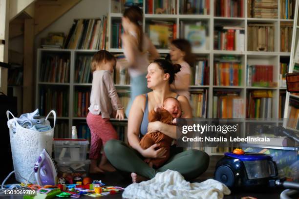 capturing maternal burnout: overwhelmed mother sitting on the floor in the living room amidst screaming baby, sibling children's activities, and household disorder - kids mess stockfoto's en -beelden