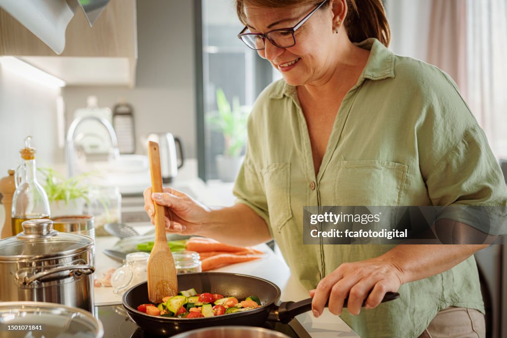 Woman cooks healthy chopped vegetables in a frying pan