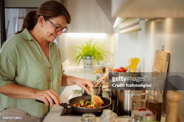 刻んだ野菜をフライパンに調理する成熟した女性 - electric stove burner ストックフォトと画像