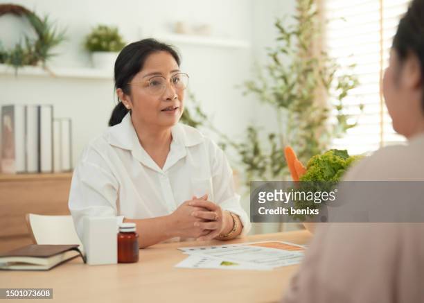 asian mature adult is giving advice on nutrition facts and health care to a obese woman. - fat loss stock-fotos und bilder