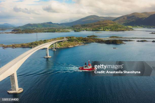 vista aérea del barco rojo navegando en el océano bajo un puente moderno en noruega - atlantic road norway fotografías e imágenes de stock