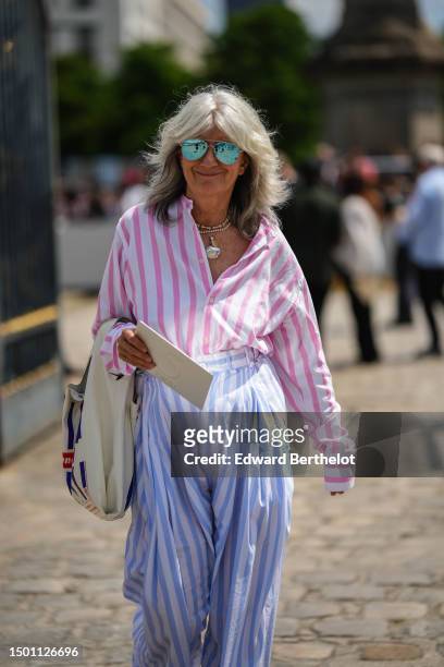 Guest wears blue aviator sunglasses, a white and pale pink striped print pattern shirt, pale blue and white striped print pattern cotton large pants,...