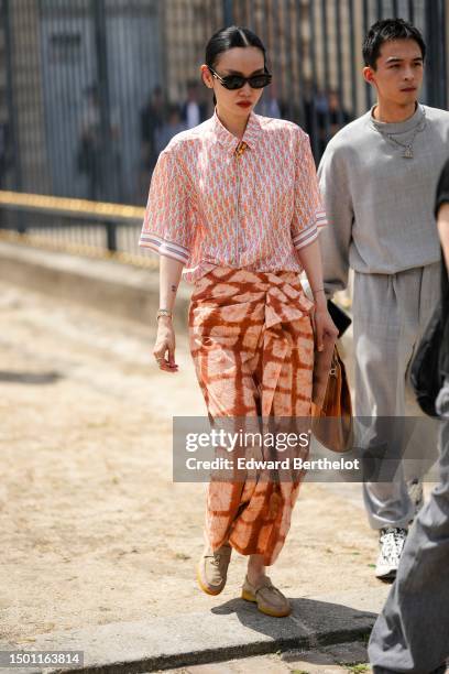 Guest wears black sunglasses from Dior, earrings, an orange with white and navy blue Dior Oblique Jacquard print pattern short sleeves silk shirt...