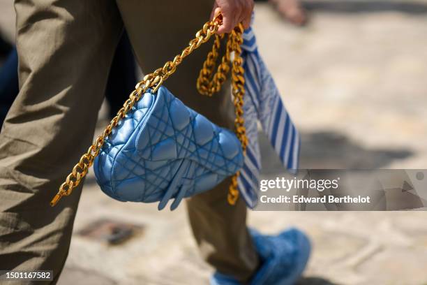 Guest wears khaki suit pants, a flashy blue shiny leather embossed quilted pattern leather Saddle handbag from Dior, blue sneakers, outside Dior,...