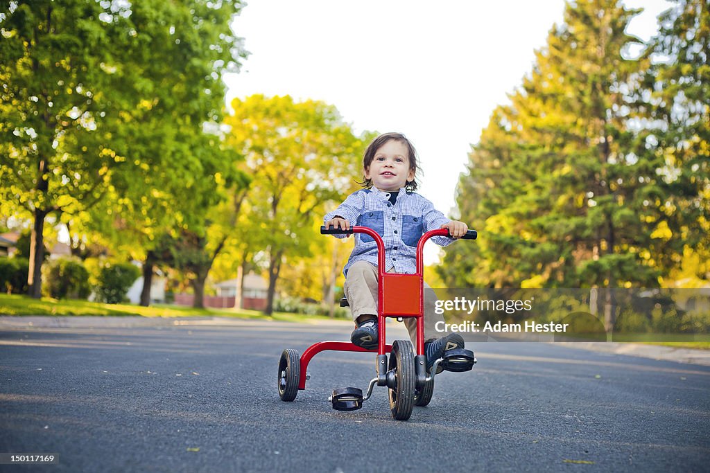 A young boy sitting on a trike outside in a street