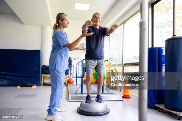 man doing exercises using a balance ball with the help of his physical therapist - ergotherapie stockfoto's en -beelden
