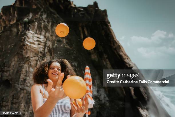 a woman juggles oranges on a sunny beach - juggling act stock pictures, royalty-free photos & images