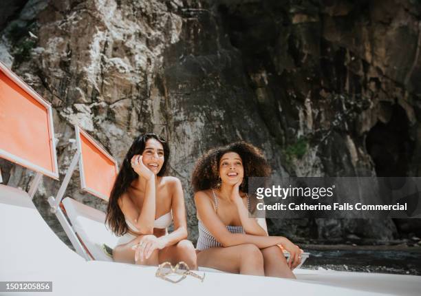 two woman share a single sun lounger on a sunny day - enjoying the beach stockfoto's en -beelden