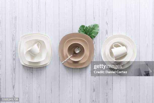 three ceramic dinner plates in shades of white and beige arranged neatly on a pristine white wooden table - tellerlift stock-fotos und bilder