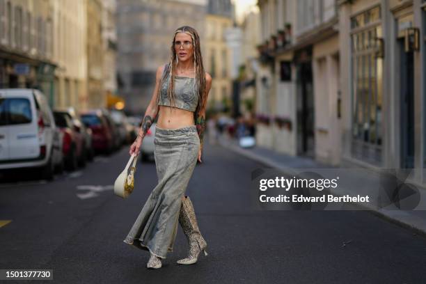 Guest wears transparent futurist glasses, a gold nose piercing, a gold chain with cross pendant necklace, a gray faded yellow denim square-neck /...