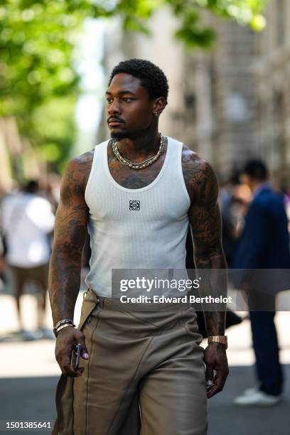 Guest wears cross pendant silver earrings, silver rhinestones necklaces, a white tank-top from Loewe, brown wrap shiny leather knees shorts, a gold...