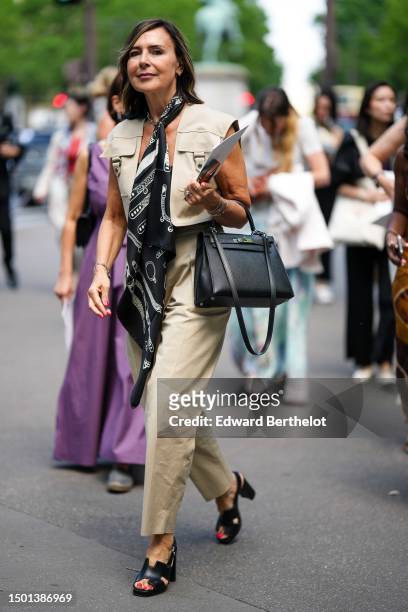Guest wears a black and white print pattern silk scarf, a beige cargo sleeveless cropped top, beige large denim cargo pants, a black shiny leather...