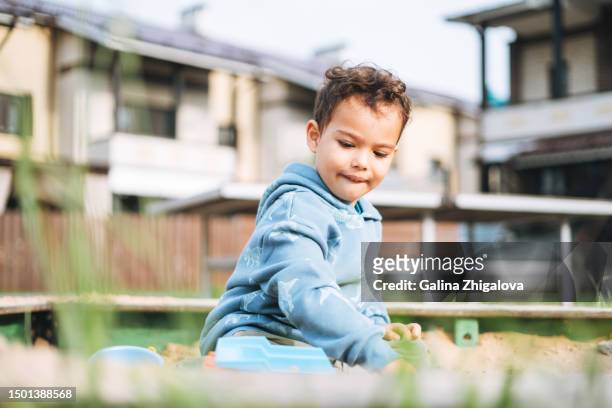little curly haired boy toddler playing in sandbox in back yard of house - 2 boys 1 sandbox stock pictures, royalty-free photos & images