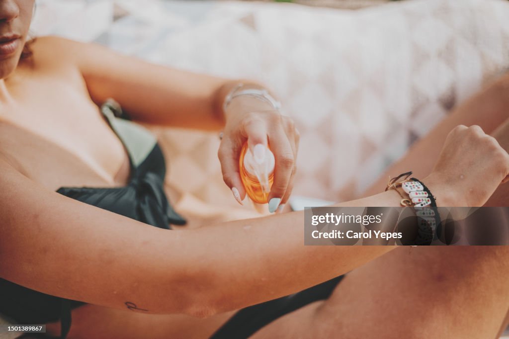 A woman spritzes sun screen on her arm during vacations