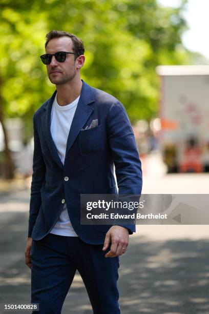 Guest wears black sunglasses, a white t-shirt, a navy blue blazer jacket, matching navy blue suit pants, outside Hermes, during the Menswear...