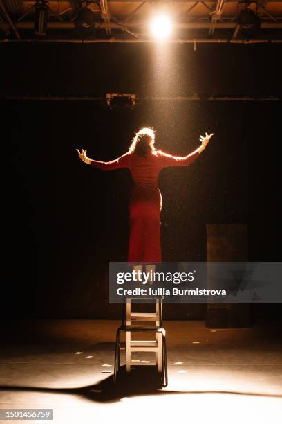 energetic young actress in old-fashioned dress standing on chair performing on stage of college drama club - musical stock-fotos und bilder