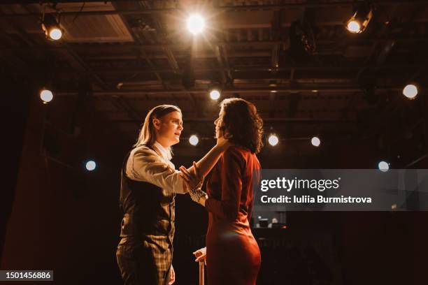 side view of woman in red dress and passionate man in suit standing face to face during emotional stage performance in drama club - dark premiere stock-fotos und bilder