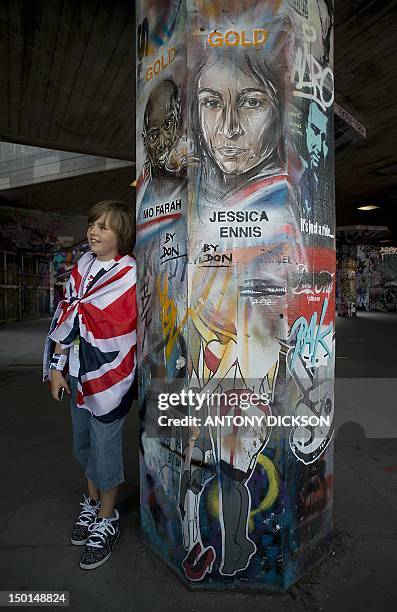 Boy draped in a Union Jack flag stands next to a mural signed by grafitti artist "Don" shows artwork of Britain's 10,000m gold medalist Mo Farah and...