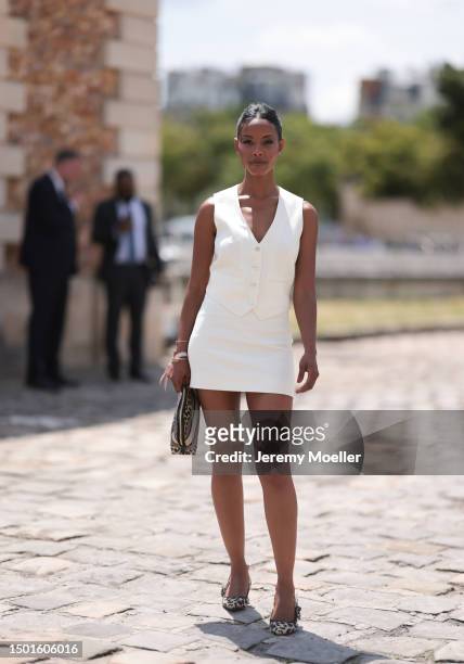 Fashion Week guest is seen wearing a creme white vest top and matching creme white mini skirt, Dior leo animal print beauty clutch and matching leo...