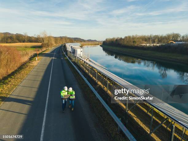aerial view two engineers using laptop next to solar power plant by river - väg och vattenbyggnadsingenjör bildbanksfoton och bilder