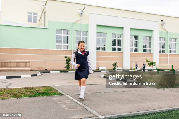 excited female student wearing school dress and bow tie walking from school building - school ground student walking stock-fotos und bilder