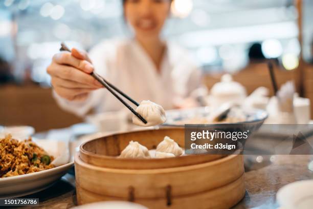 young asian woman eating steamed dumpling with chopsticks with assorted dishes freshly served on the table in a chinese restaurant. asian chinese food and culture. people, food and lifestyle - momo stock pictures, royalty-free photos & images