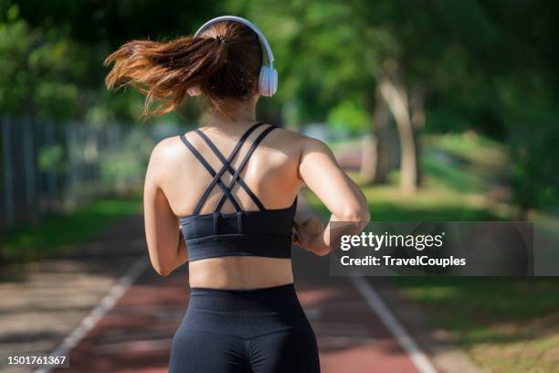 young fitness sports women runner running in the park. happy athletic woman listening music on earphones while running in nature in the morning. healthy fitness woman jogging outdoors. - dorsal fin stock photos et images de collection