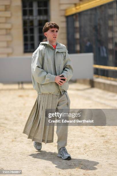 Guest wears a neon orange t-shirt, a pale gray zipper hoodie rain coat, pale gray pleated / accordion long train skirt pants from Dior, gray leather...