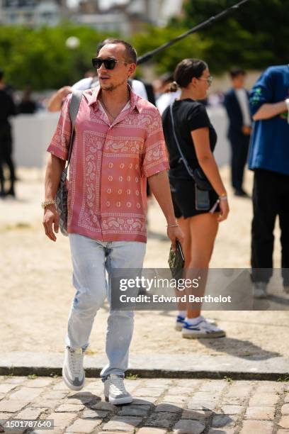 Guest wears black sunglasses, a pale red with embroidered white print pattern short sleeves shirt, a gray print pattern in coated canvas shoulder bag...