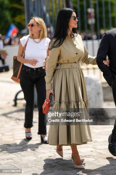 Guest wears black sunglasses, a beige buttoned shirt from Dior, a matching beige pleated ruffled midi skirt from Dior, a red shiny leather micro Lady...