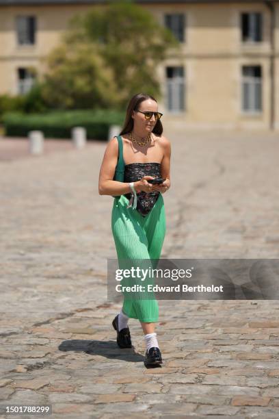 Guest wears black sunglasses, a gold chain with black logo pendant necklace from Chanel, a gold large circles necklace, a black with red / yellow /...