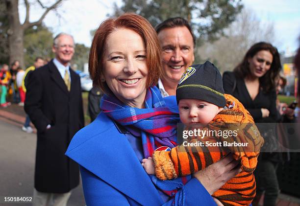 Australian Prime Minister Julia Gillard is watched by her partner Tim Mathieson as she holds a baby dressed in the colours of the Richmond Tigers as...